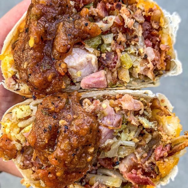 A large burrito, cut in half, revealing a filling of meat, eggs, and salsa.