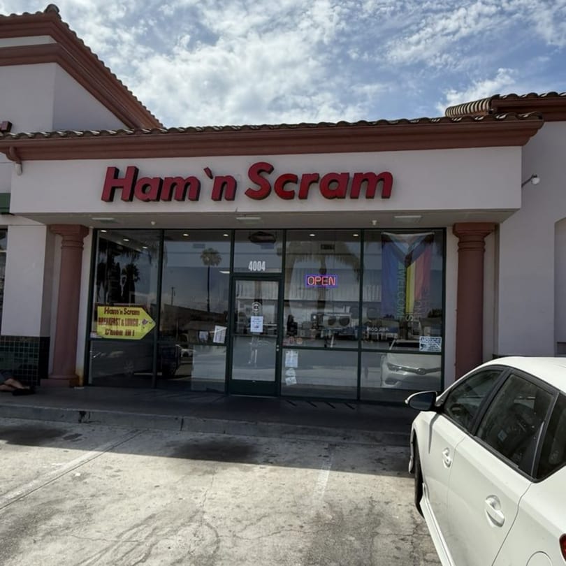 Exterior of Ham'n Scram restaurant with a red sign, glass storefront, and a white car parked outside.