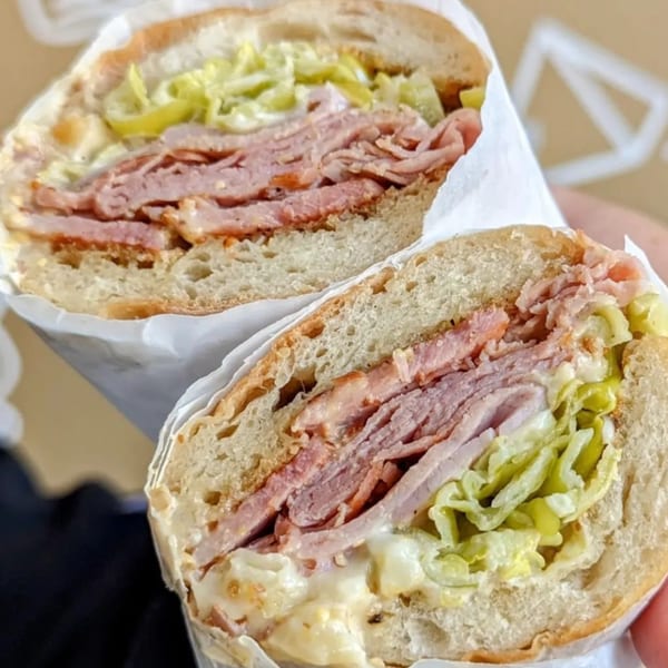 Two halves of a large sandwich with deli meat, shredded lettuce, and sauce on a hoagie roll.