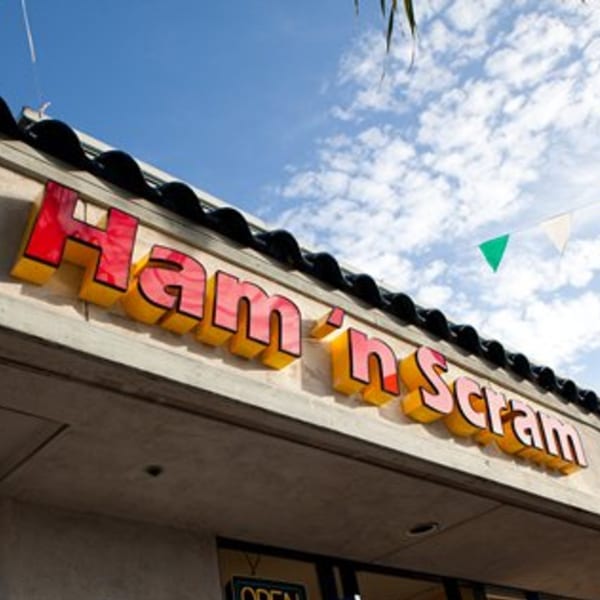 The red and yellow "Ham 'n Scram" sign on a building under a blue sky with clouds.