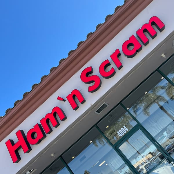 The red "Ham 'n Scram" sign on a white building with a brown tiled roof under a blue sky.