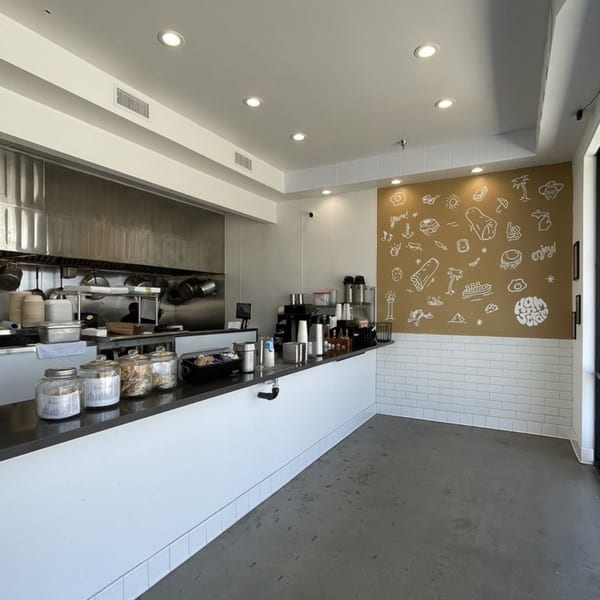 Modern restaurant interior with a long counter, kitchen in the background, and a wall mural.