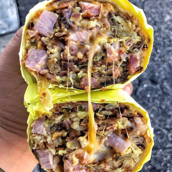 A breakfast burrito, cut in half, revealing melted cheese, ham, and scrambled eggs.