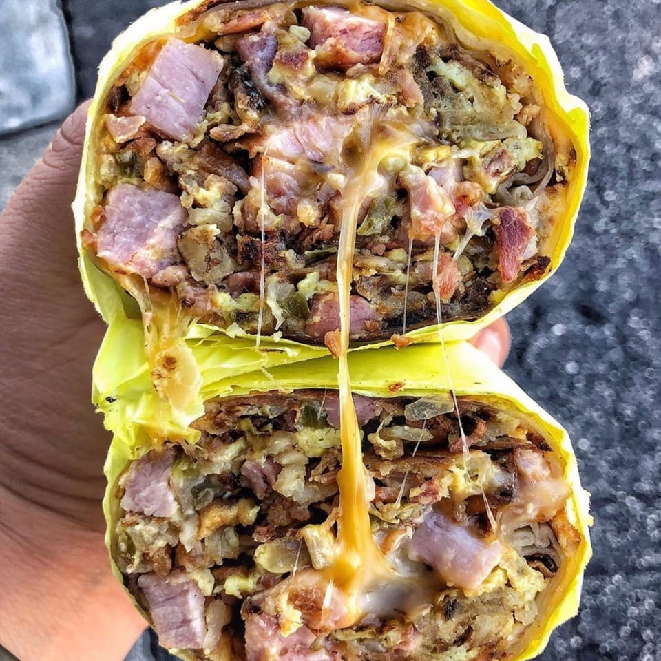 A breakfast burrito, cut in half, revealing melted cheese, ham, and scrambled eggs.
