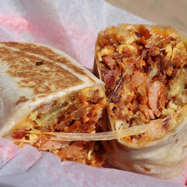 A large burrito, cut in half, revealing a savory filling of meat, eggs, and cheese.